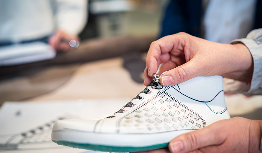Nahaufnahme einer Person, die an einem Schuhprototyp mit kreativem Design arbeitet.