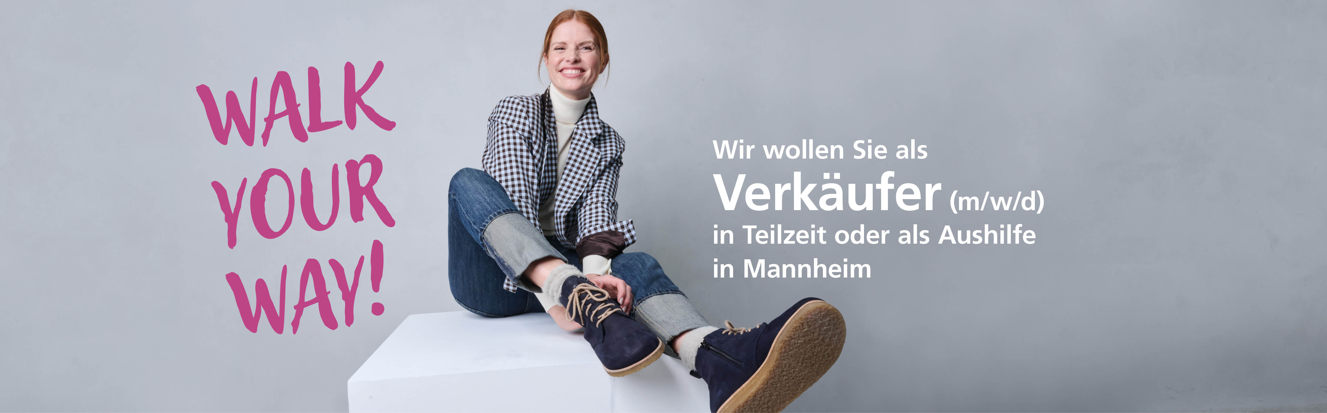 Lächelnde Frau in legerer Kleidung sitzt neben Text: 'Walk Your Way'. Verkäufer gesucht in Mannheim.