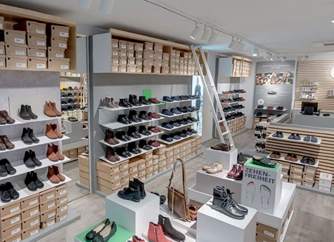 Innenansicht eines modernen Schuhgeschäfts mit Regalen voller Schuhe und Leitern zum Erreichen höherer Ebenen