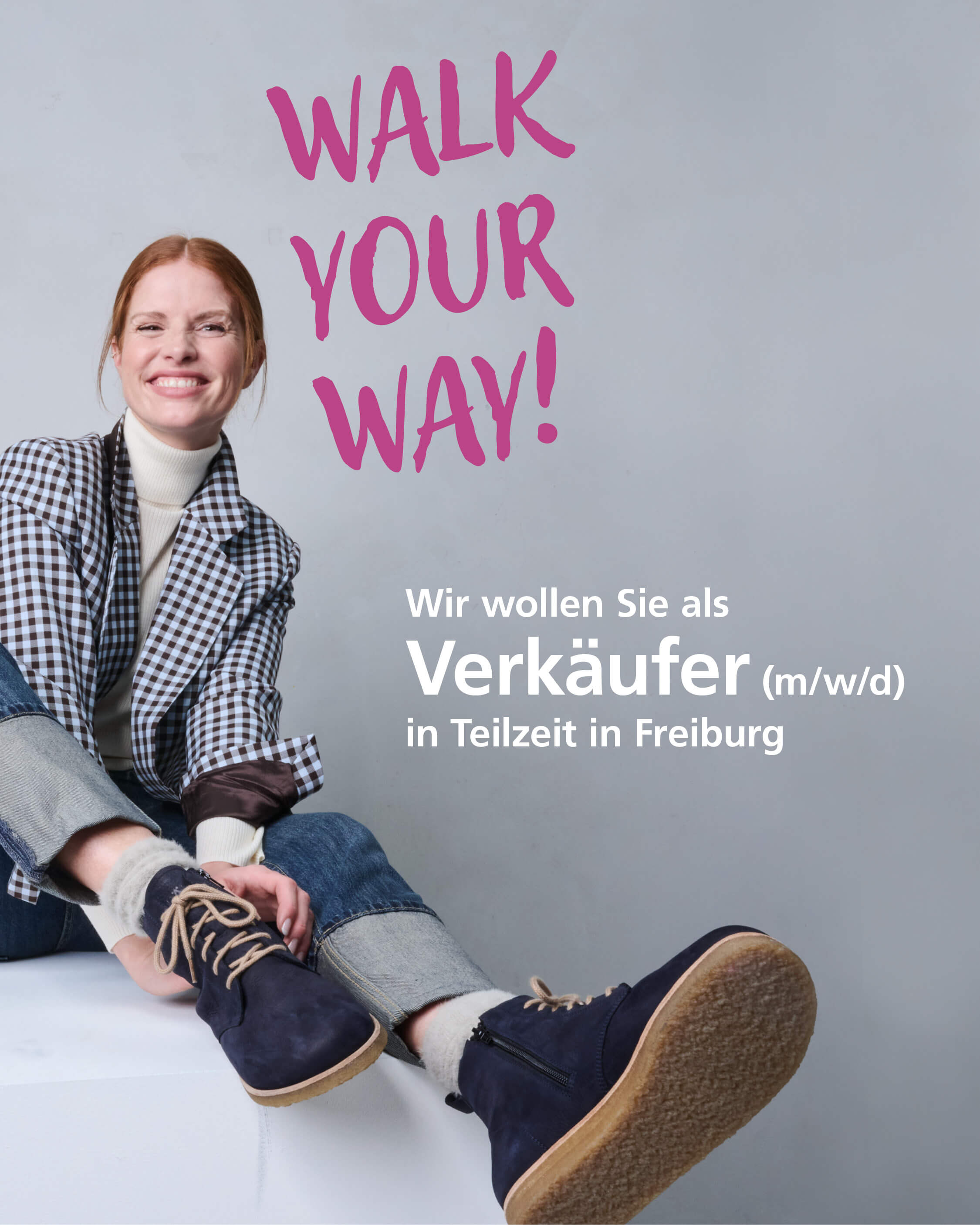 Junge Frau in kariertem Blazer und Jeans präsentiert eine Werbeanzeige für einen Teilzeit-Verkäufer (m/w/d) in Freiburg mit dem Slogan 'Walk Your Way!'