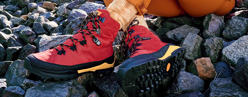 Nahaufnahme von roten Wanderschuhen mit robuster Sohle auf steinigem Boden