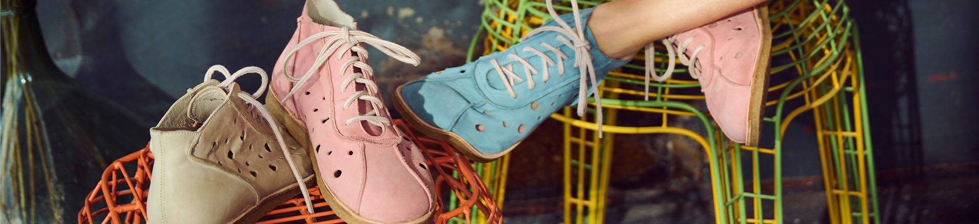 Bequeme Kinderschuhe in Pastellfarben mit Schnürsenkeln und Lochmuster auf bunten Stühlen