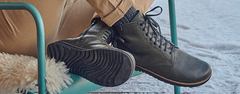 Person trägt schwarze Lederstiefel und sitzt auf einem blauem Stuhl im Schnee