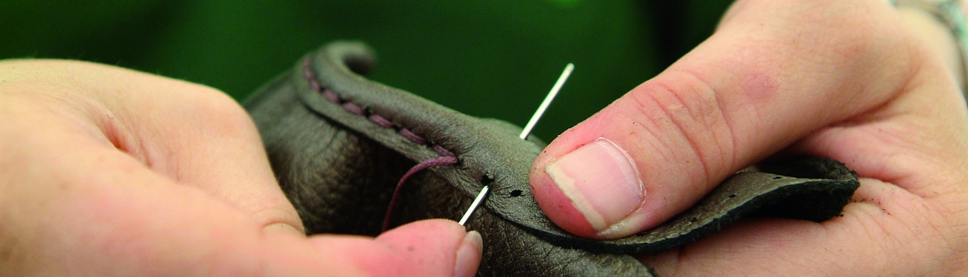 Nahaufnahme einer Hand, die Leder mit einer Nadel und Faden näht