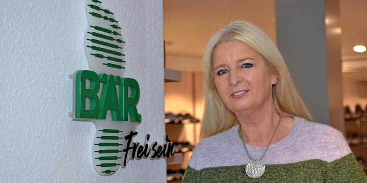 Blonde Frau steht lächelnd vor dem BÄR-Schriftzug in einem Schuhgeschäft